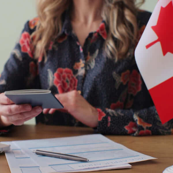 Một người đang cầm cuốn hộ chiếu Canada với lá cờ Canada ở phía sau.