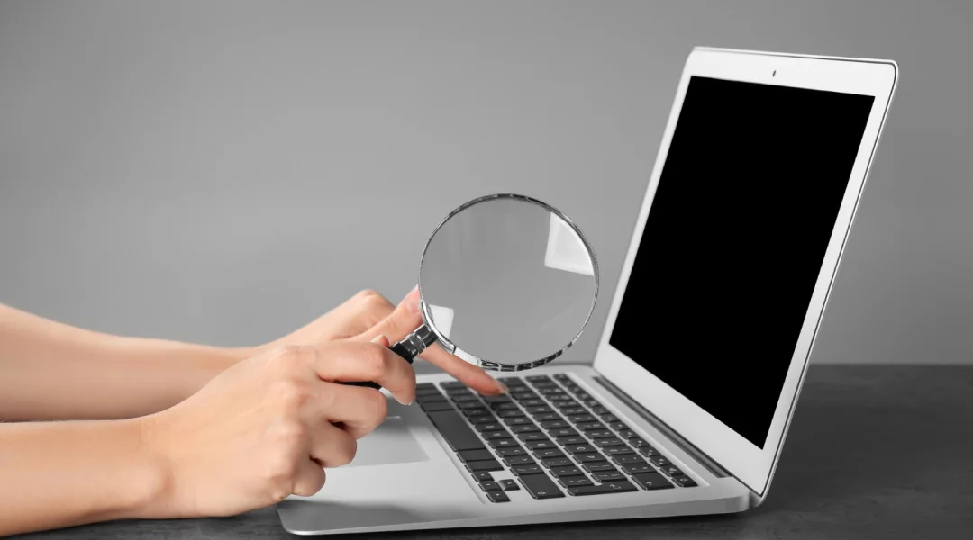 A person examines a laptop screen with a magnifying glass, searching for job opportunities for Vietnamese individuals.