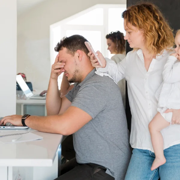 A man and woman with a baby sit at a desk with a laptop, discussing their plans to sponsor a family to Canada.