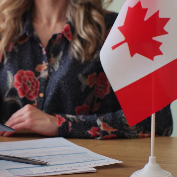 A woman sitting at a desk with a Canadian flag, focused on obtaining a work permit for Canada.