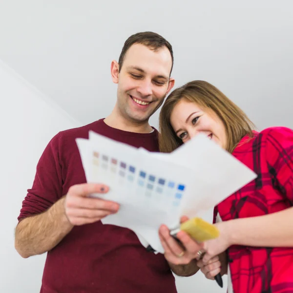 A man and woman examine a paint sample together, discussing colors for their home as part of a family sponsorship initiative.