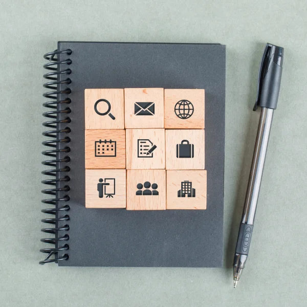Wooden cubes with icons placed on a notebook beside a pen, symbolizing the process of applying for a Canadian student visa.